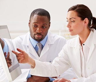 Man and woman in lab coats looking at computer screen